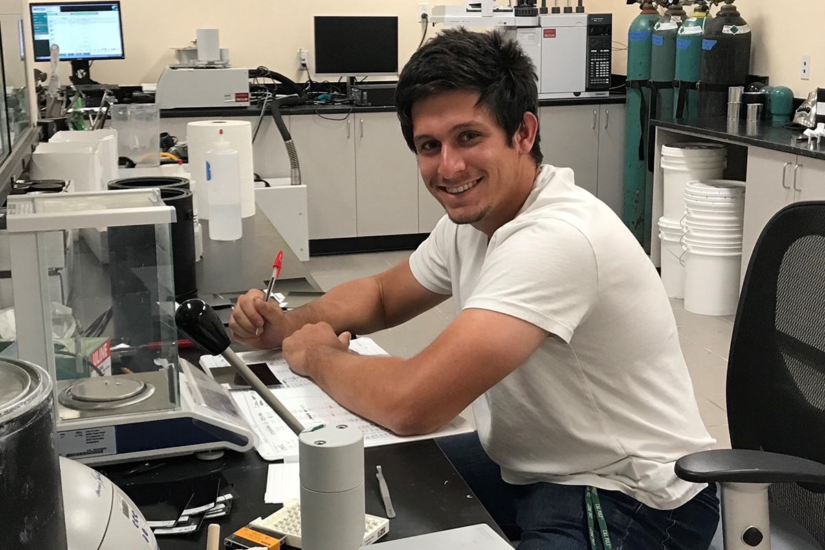 Chemistry graduate student Adam Langevin records data at a lab bench surrounded by scientific instruments and equipment.