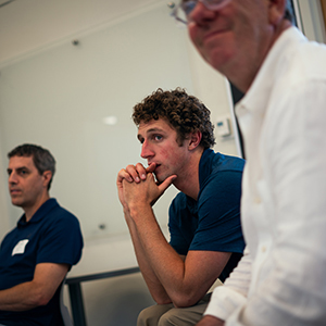Three men seated in a classroom, listening to an event discussion. McClain Kressman is in the center leaning forward, with his hands clasped while listening.