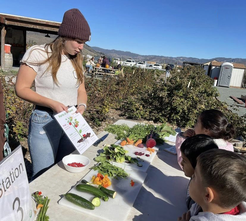 Cal Poly nutrition major Rairaja Cohen teaches young students about parts of a plant during an outdoor garden activity.