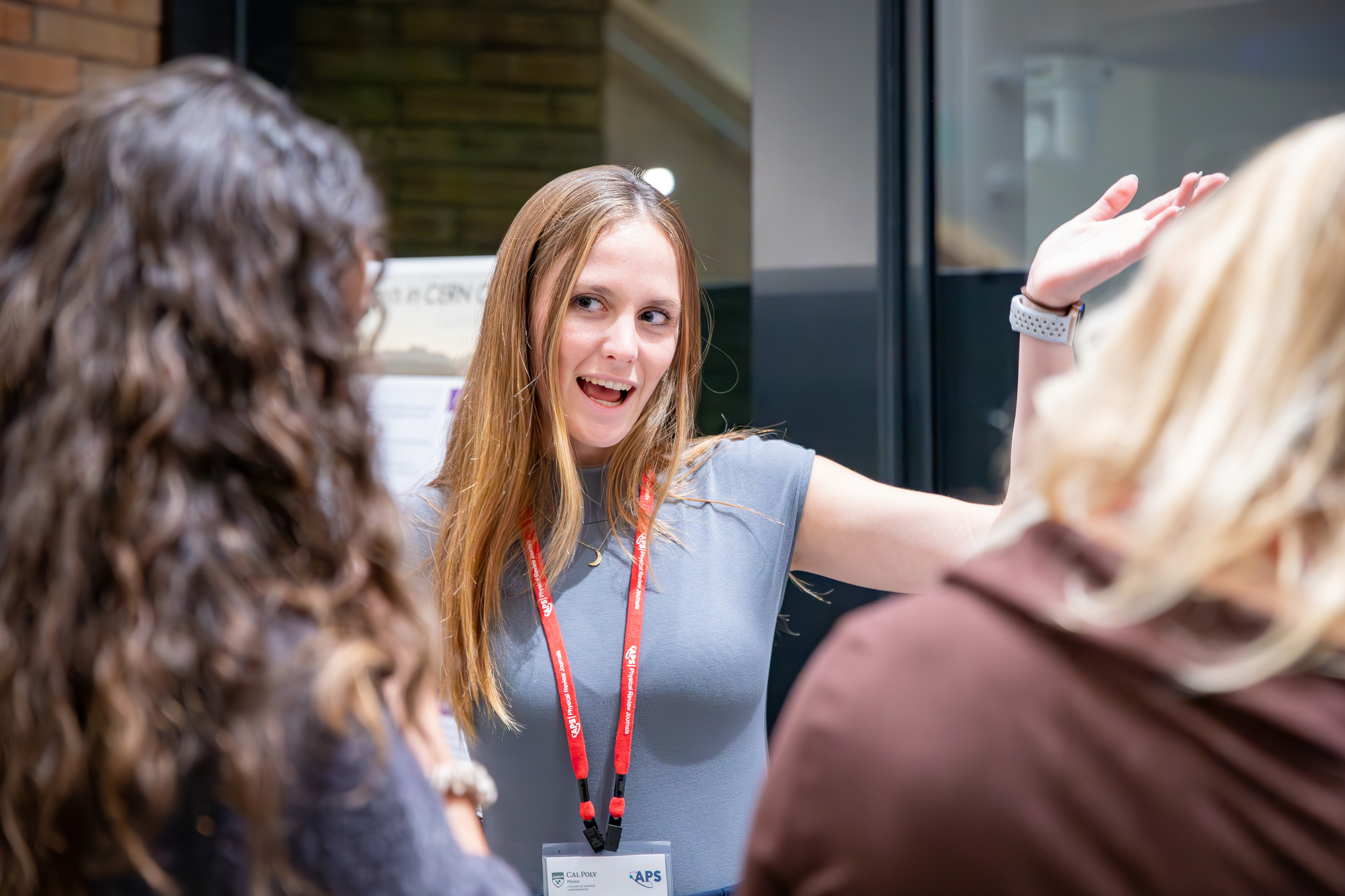 A student presents research and gestures while speaking with other attendees during the APS Conference for Undergraduate Women and Gender Minorities in Physics at Cal Poly.