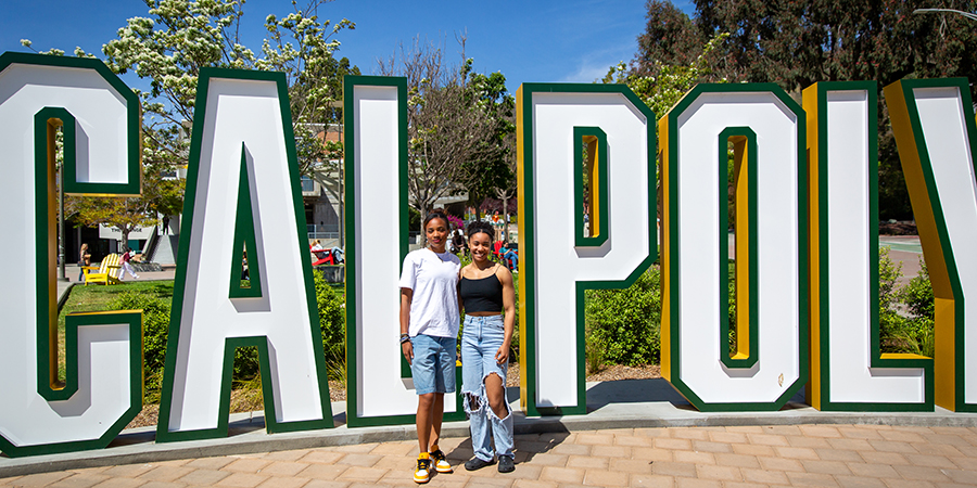 Sisters Maya Glover (left), an architecture major, and Genesis Glover (right), a biological sciences major, stand together on a walkway in front of the the Cal Poly letter installation near the University Union Plaza.