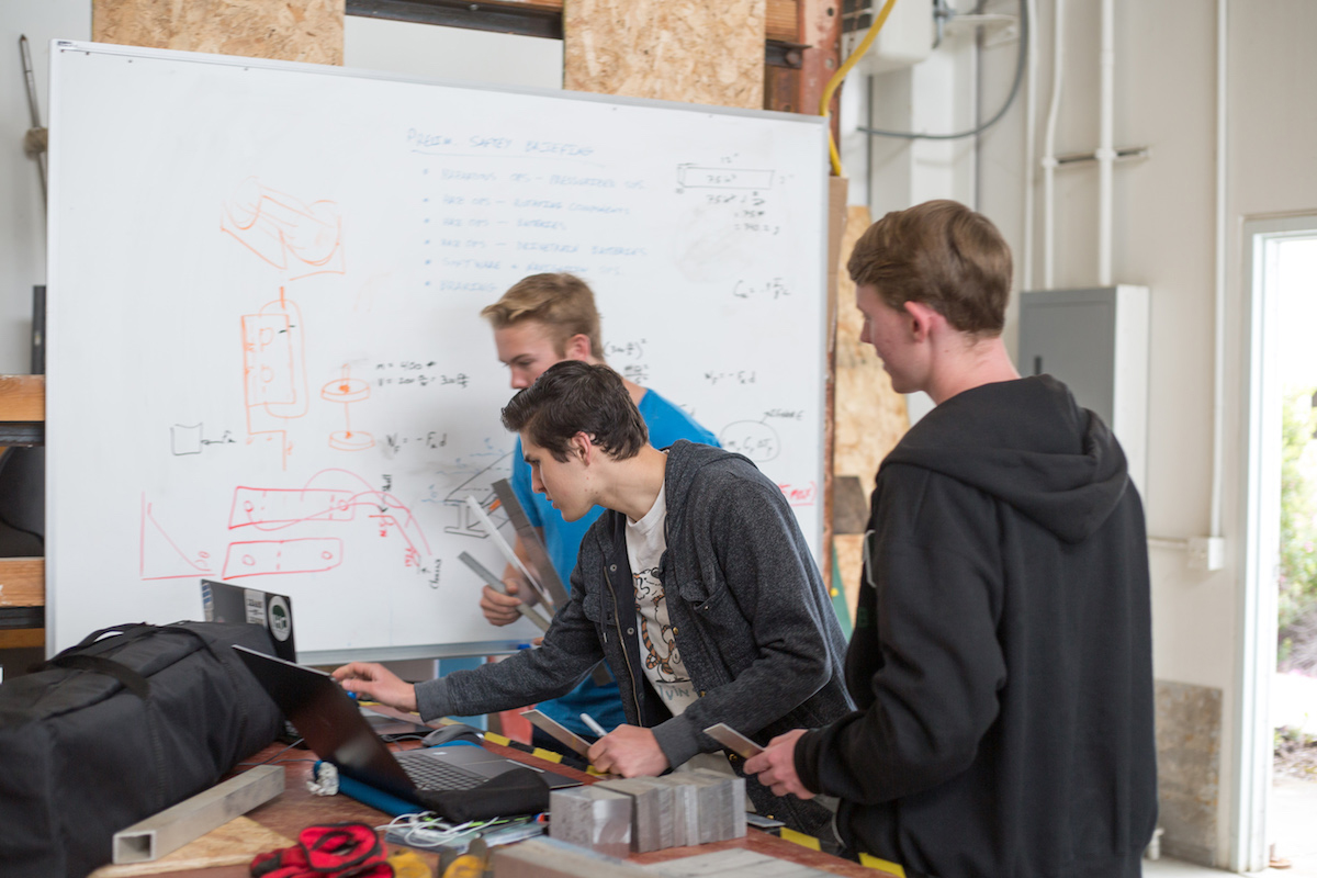 Students gather around a white board to workout problems for their prototype.