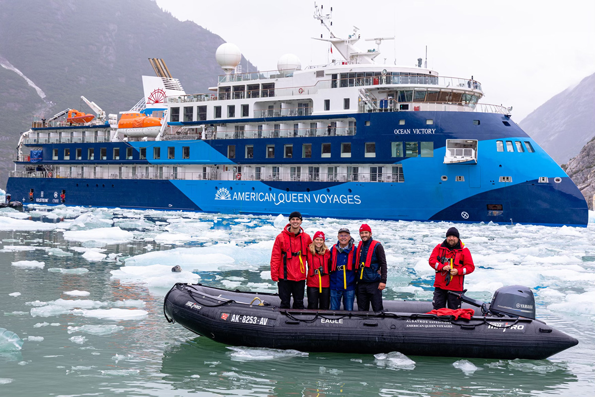 Researchers stand in an inflatable boat among ice floes with the expedition ship Ocean Victory behind them during polar fieldwork.