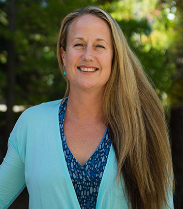 Cal Poly biological sciences professor Emily Taylor smiles in an outdoor portrait with trees in the background.
