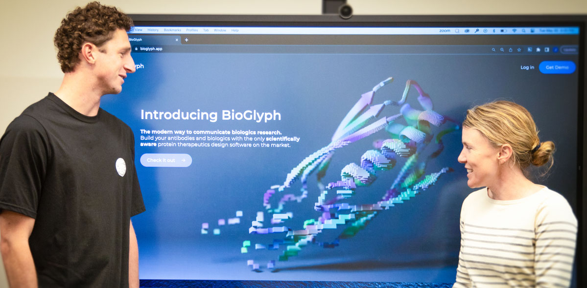 McClain Kressman and Professor Jean Davidson standing in front of a large screen presentation explaining BioGlyph.