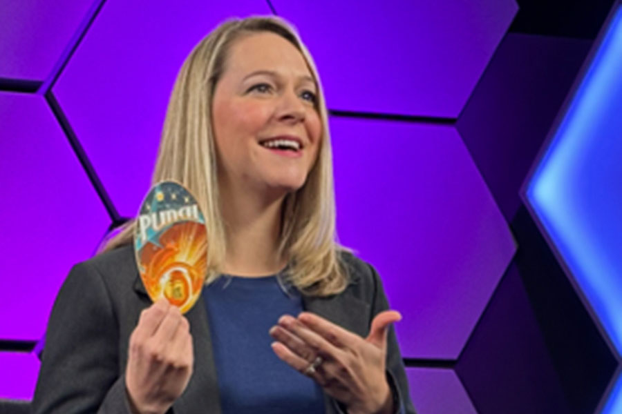 NASA PUNCH scientist Nicholeen Viall speaking onstage while holding a small illustrated card, standing in front of a purple geometric backdrop.