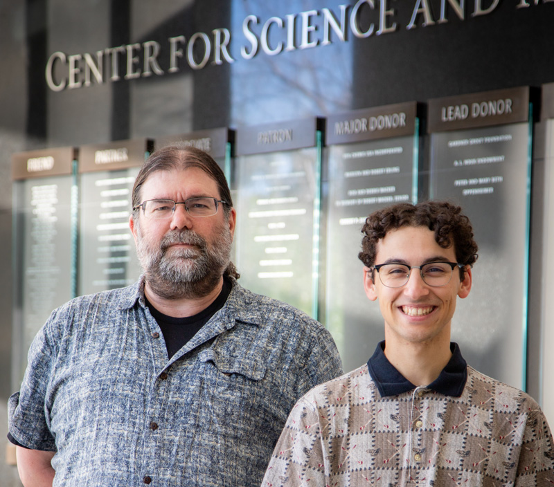 Mathematics Professor Charles David Camp and student Rapha Coutin standing in front of donor wall Cal Poly’s Center for Science and Mathematics.