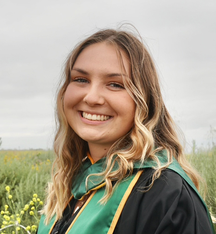 Portrait of Lia Roccucci in cap and gown standing outdoors in a field.