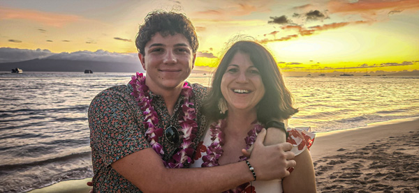 Jeff Wilson hugging his mother Katrina, both wearing leis and standing on a beach at sunset. 