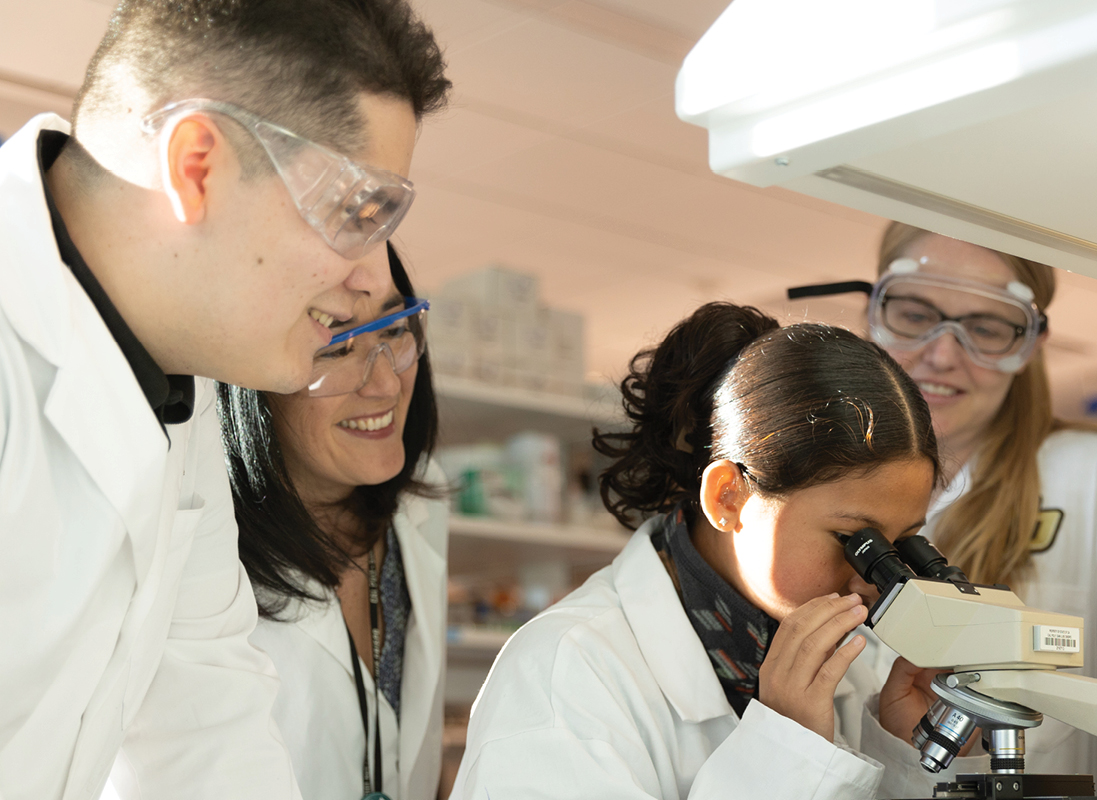Nuestra Ciencia researchers teach elementary student to use microscope.