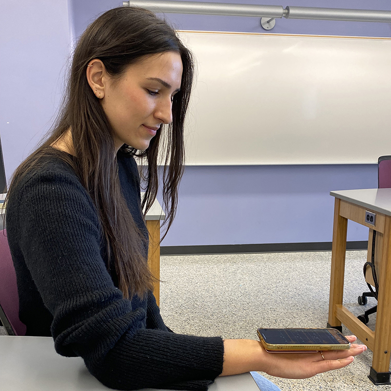 A student balances a smartphone flat on her palm while demonstrating a physics activity that uses the phone’s sensors to measure motion.