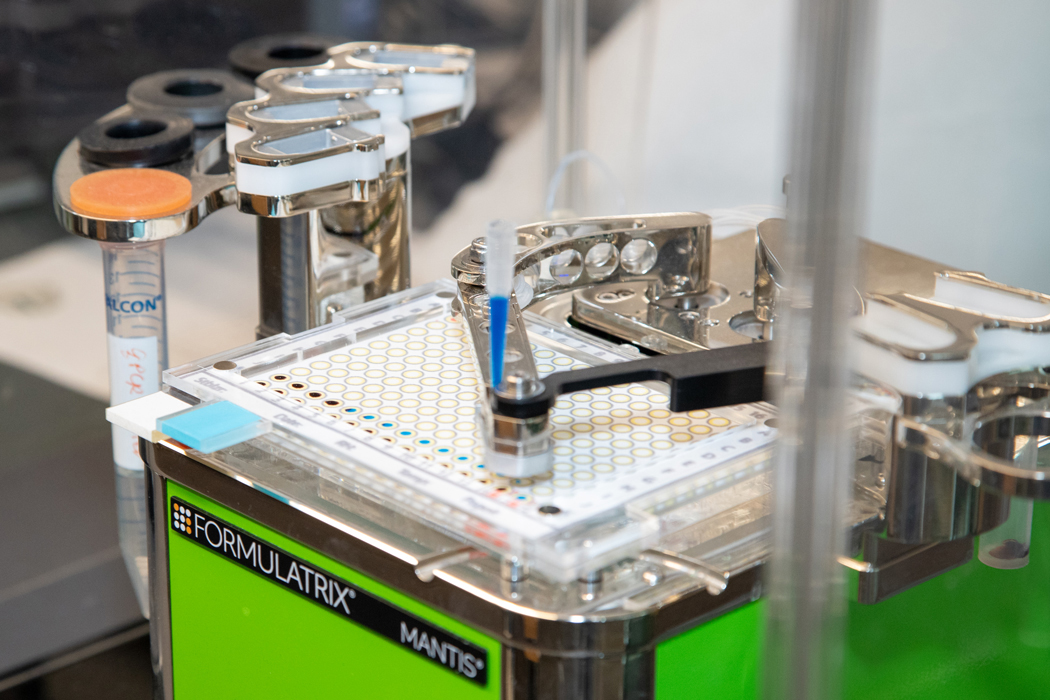 Close-up of an automated laboratory device dispensing liquid into a multi-well plate used for diagnostic testing experiments.