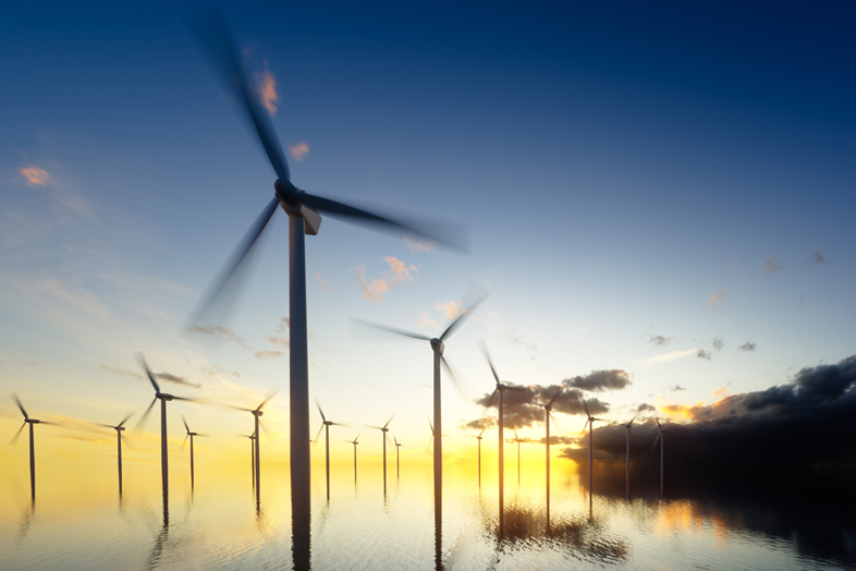 Wind turbines in offshore wind farm at sunset, with multiple turbines standing in calm water and their blades rotating against a colorful sky.