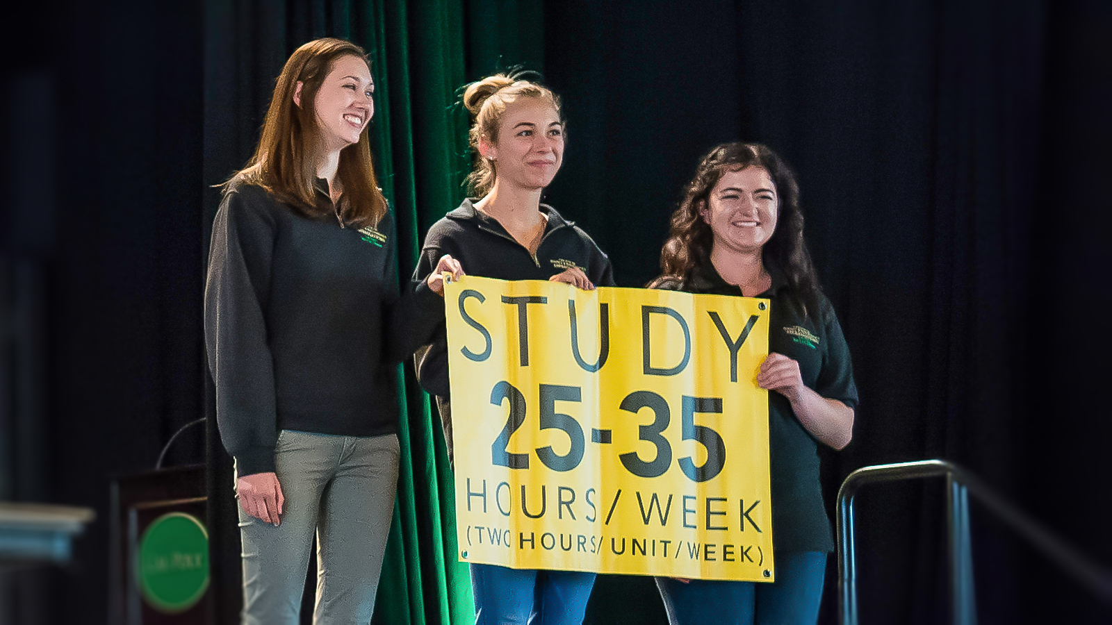 Bailey College Open House student volunteers on stage with Study 25-35 sign.