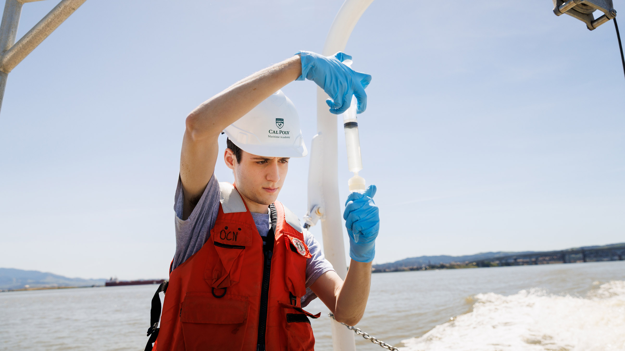 Cal Poly Maritime Academy oceanography student examines syringe on a boat