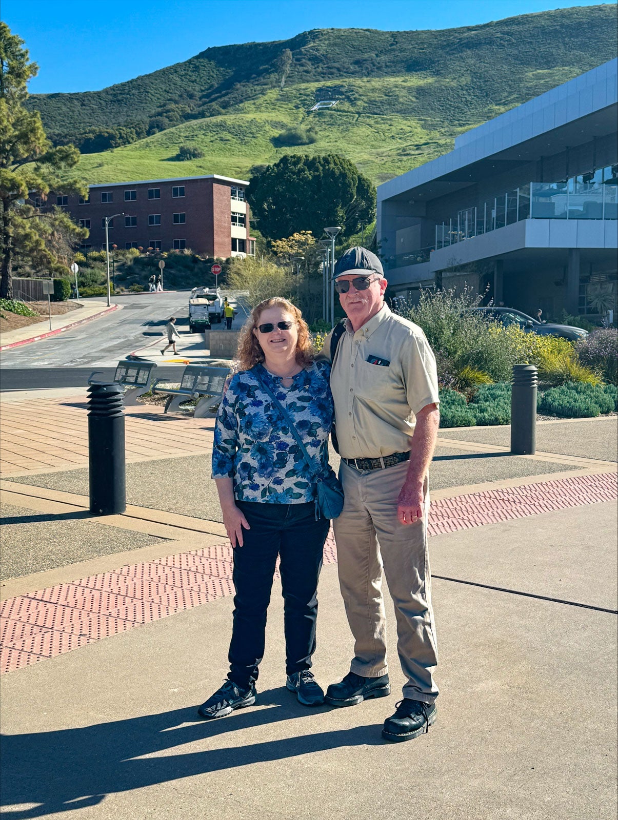 Mark and Marley Kent pose on the Cal Poly campus. The Cal Poly "P" is visible on the hill behind them.