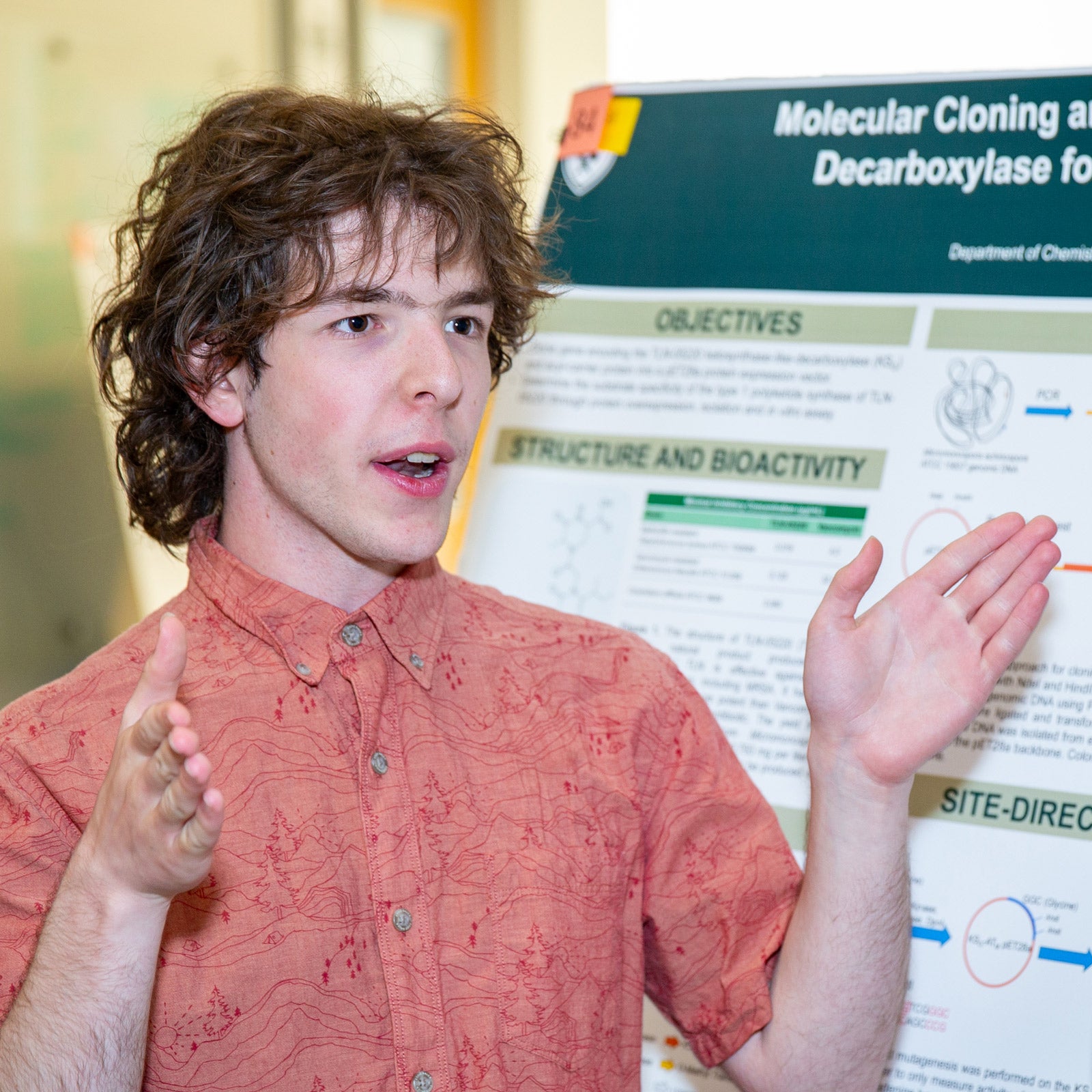 Frost Scholar alum Sam Catania stands in front of his research poster explaining his research.