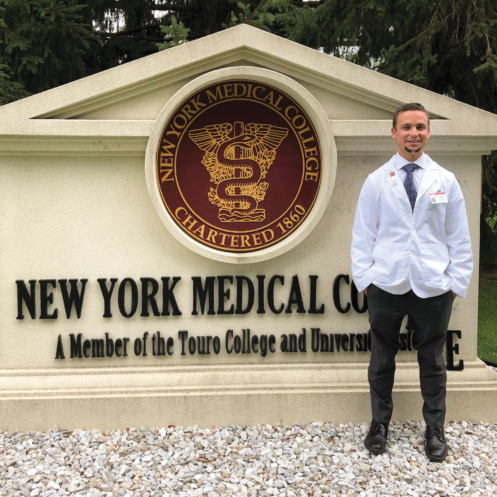 Frost Scholar alum Jake Voss poses in a medical coat in front of the sign for New York Medical College.