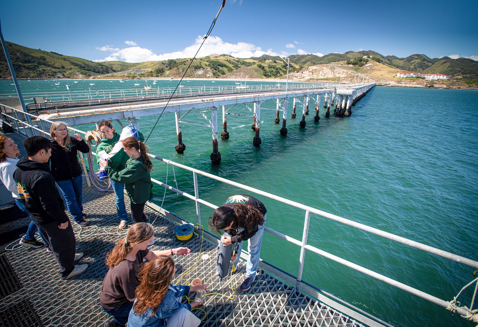 A number of students engage in research using specialized tools at the edge of the pier.
