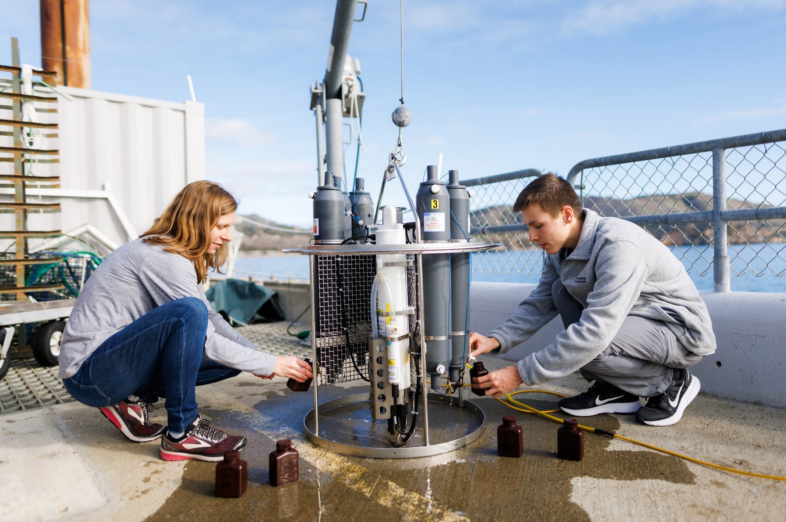 A professor and student kneel next to a conductivity, temperature, and depth profile at the Cal Poly pier.