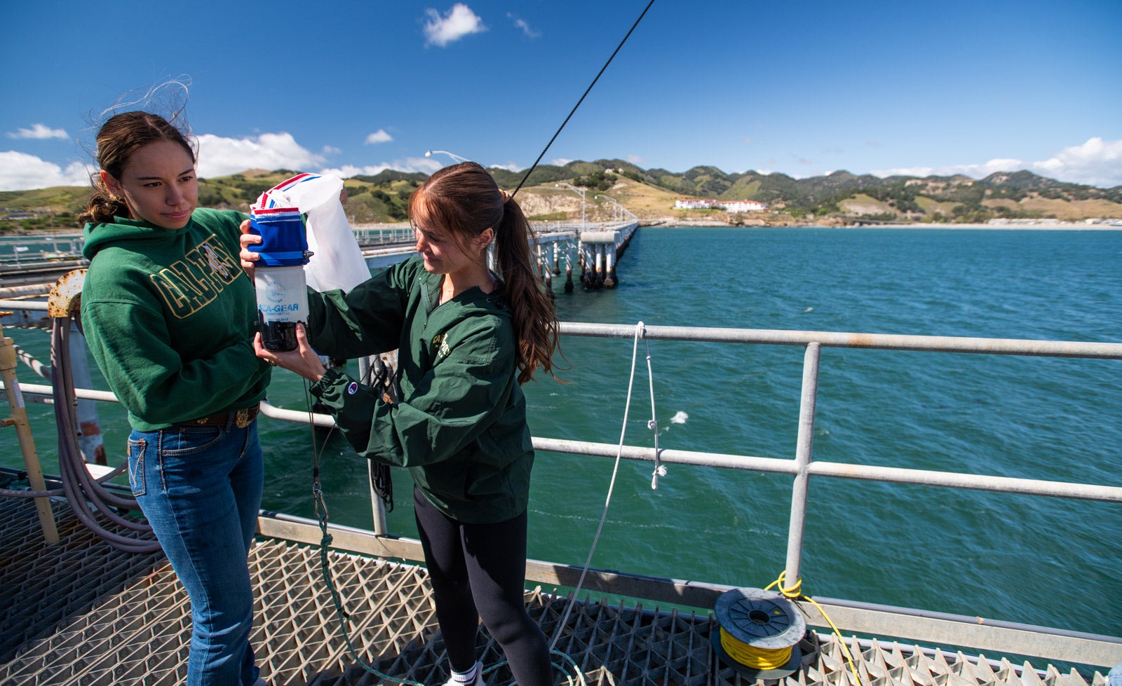 Two Cal Poly students hold a plankton net at the edge of the pier.