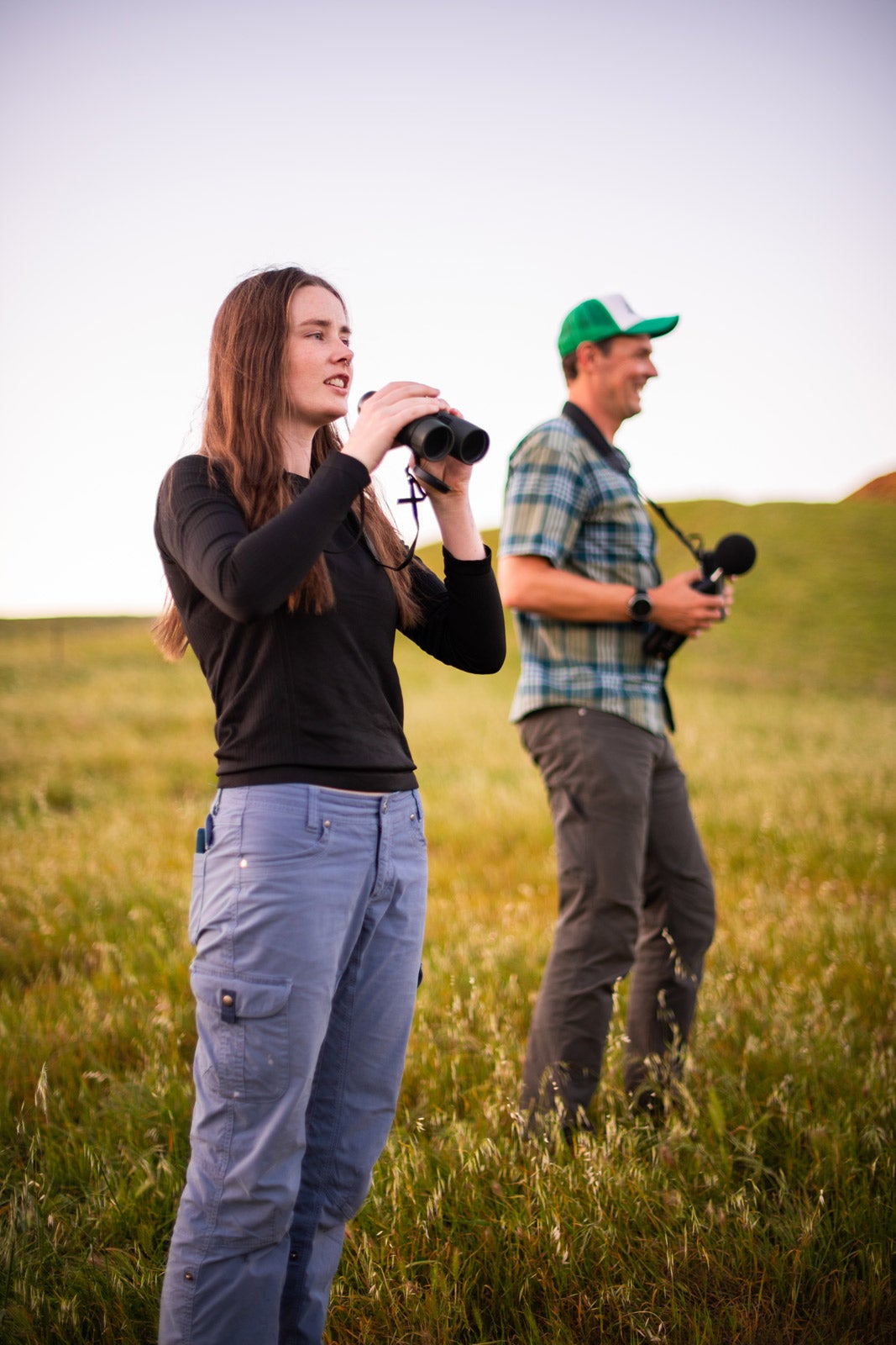 Biology master's student Eva Moylan stands with professor Clinton Francis in Poly Canyon, each holding binoculars
