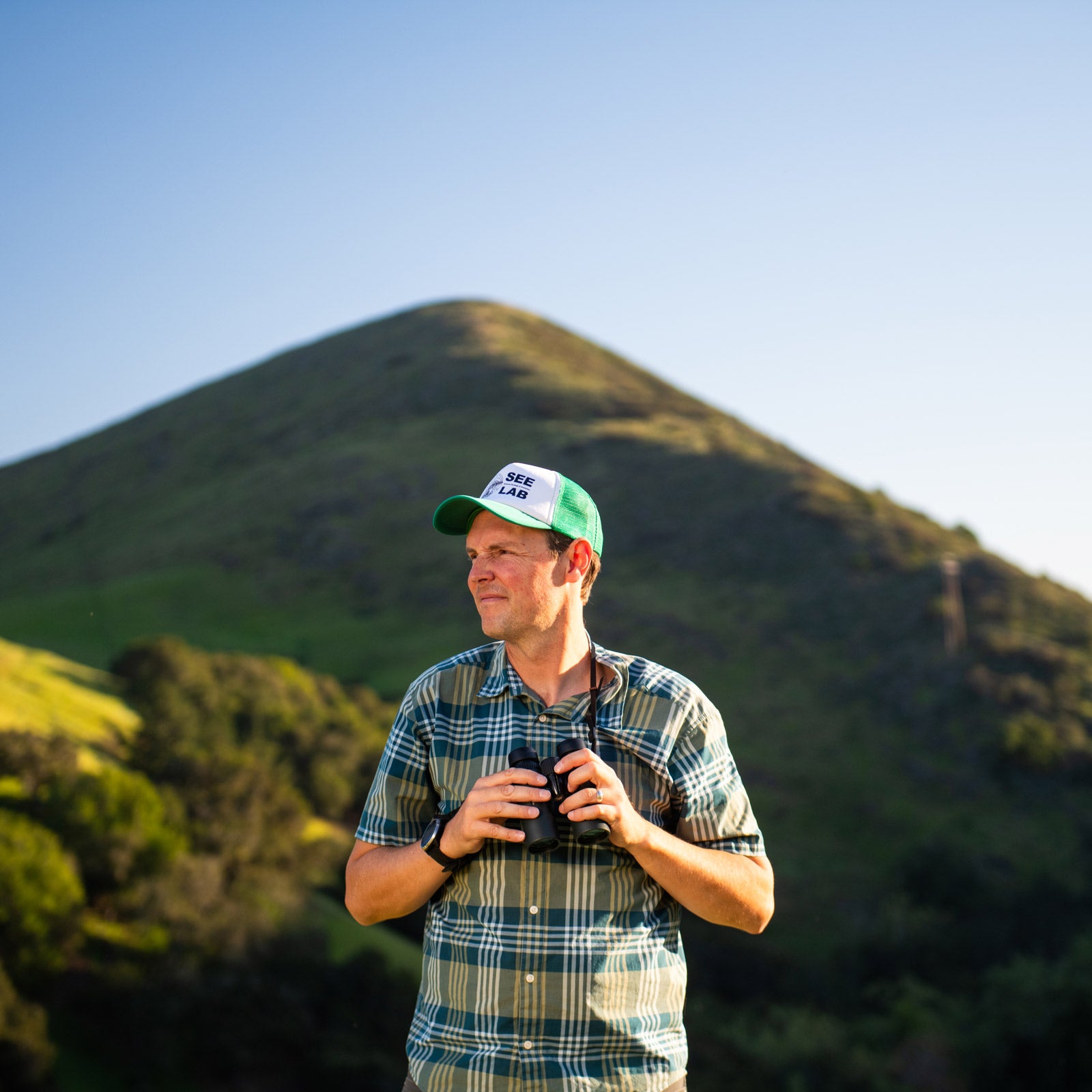 Biological sciences professor Clinton Francis stands in Poly Canyon holding binoculars