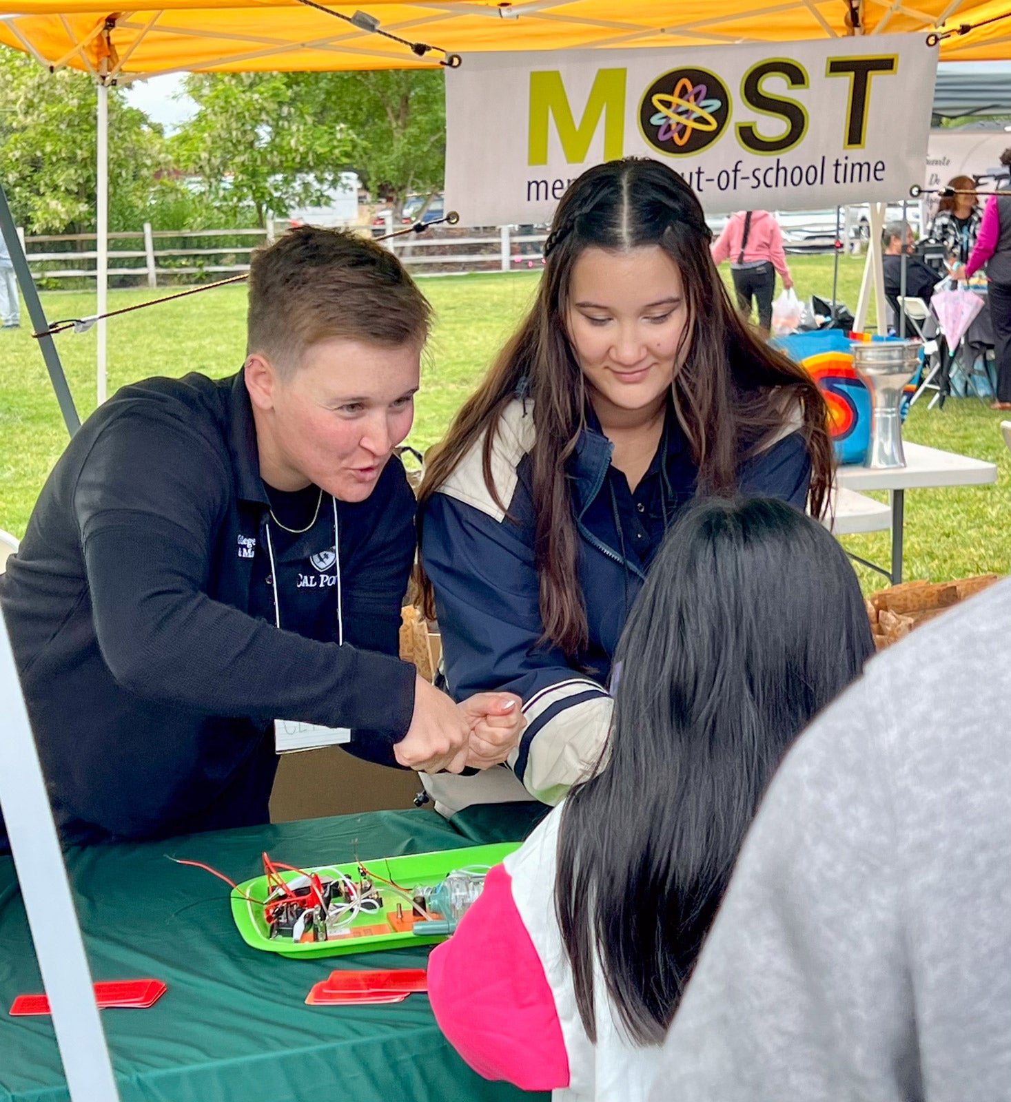 Claire Gillaspie and Ellie Farrar lead a circuit exploration activity on a table outside, speaking to children.