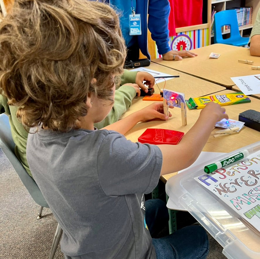 An elementary school student practices building simple circuits in a classroom.