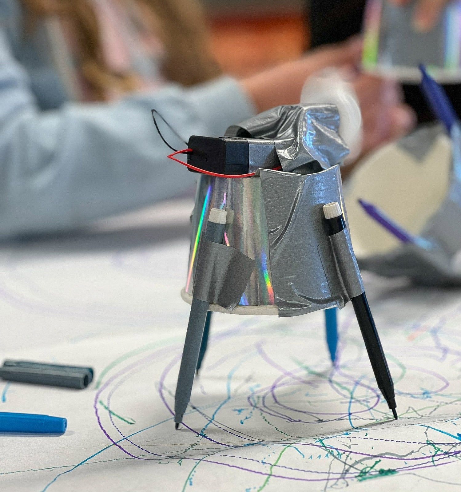 A simple drawing machine made from a paper cup, pens, tape, and a simple circuit.