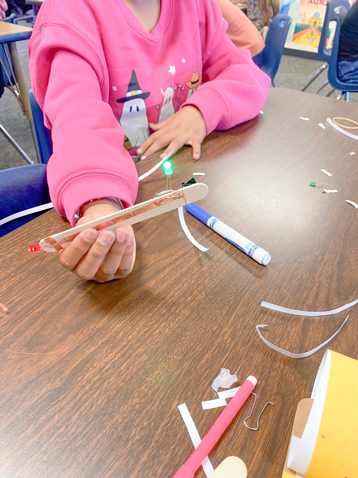 A child showing their circuit made of a popsicle stick, copper tape, wire, a coin cell battery and LED lights.