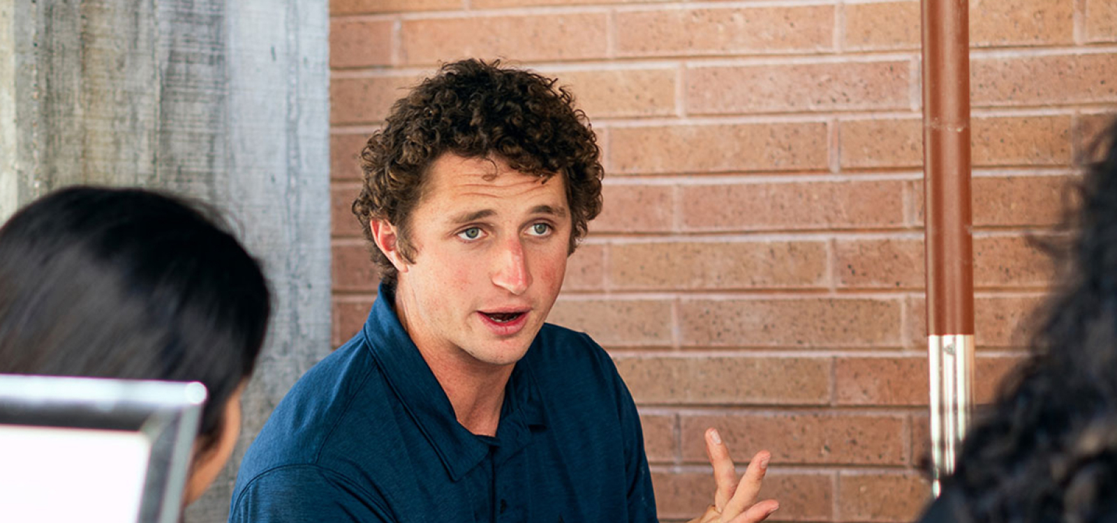 Cal Poly alumnus and biotechnology startup co-founder McClain Kressman speaking to a small audience in a classroom while standing near a projection screen.