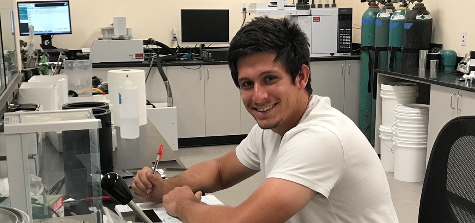 Chemistry graduate student Adam Langevin records data at a lab bench surrounded by scientific instruments and equipment.