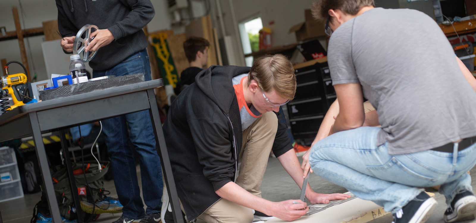 Three students taking measurements and cutting wood.