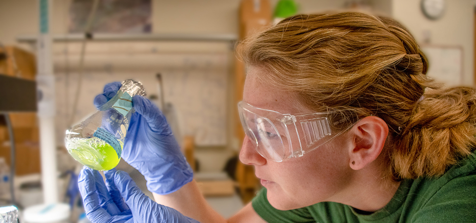 Biological sciences student Haley Edwards looks closely at a small vial of green algae culture while working at a lab bench in the Keeling Lab.