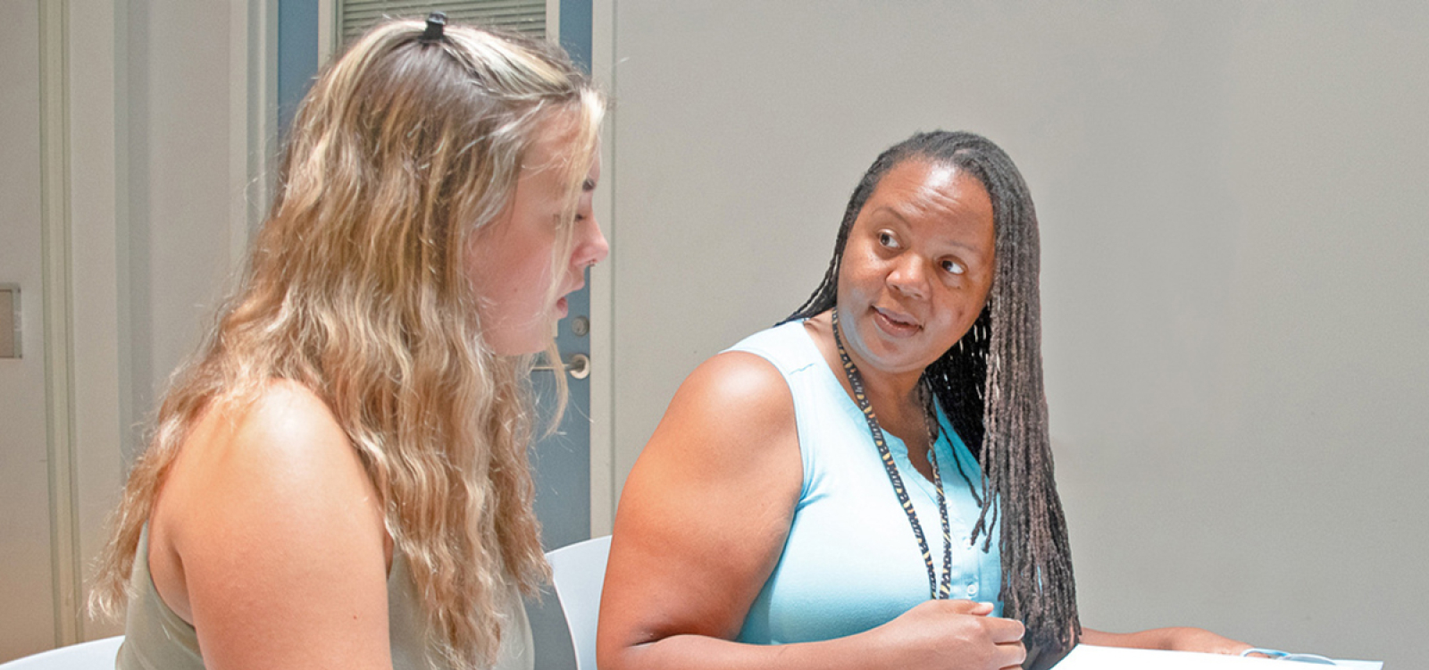 A Cal Poly professor and student sit at a table reviewing materials in a binder, discussing research during a meeting in a classroom.