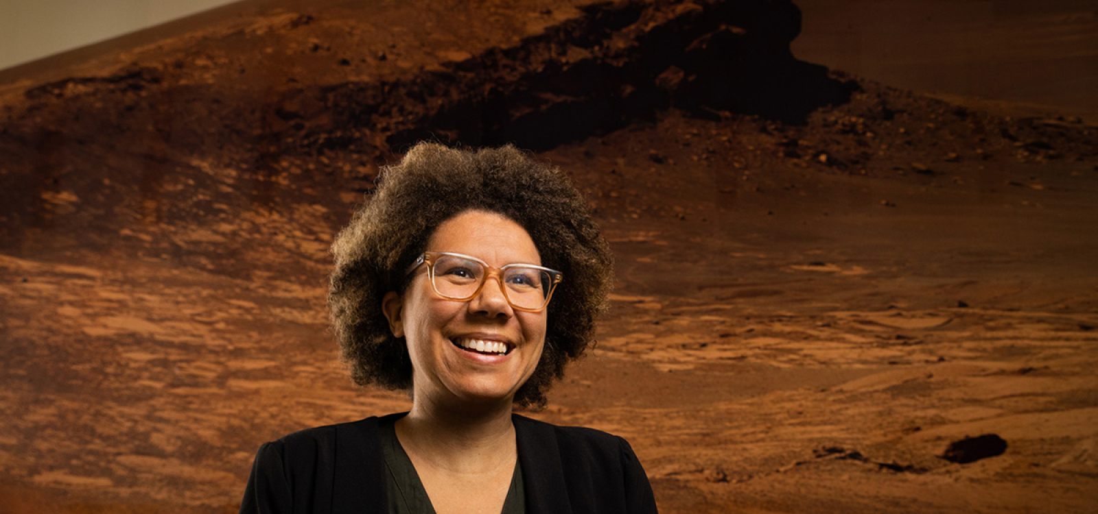 Astronomy professor Louise Edwards stands in front of a large wall mural showing the surface of Mars inside the Baker Center for Science and Mathematics.