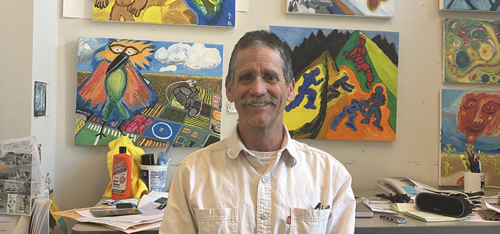 Physics Professor Tony Garcia, who specializes in geology, poses in his office with his art work in the background.