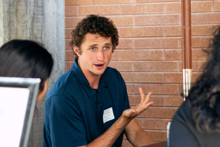 Cal Poly alumnus and biotechnology startup co-founder McClain Kressman speaking to a small audience in a classroom while standing near a projection screen.