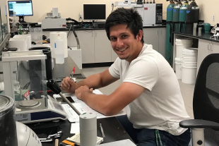 Chemistry graduate student Adam Langevin records data at a lab bench surrounded by scientific instruments and equipment.