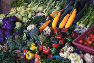 Display of fresh vegetables at a market stall, including zucchini, yellow squash, peppers, broccoli, cauliflower, cabbage and tomatoes.
