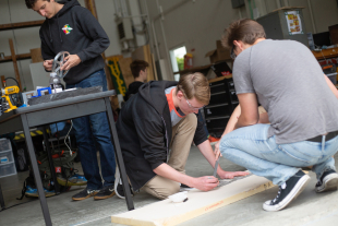 Three students taking measurements and cutting wood.