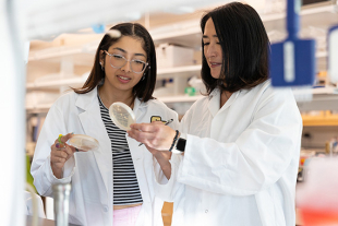 Biology professor Alejandra Yep standing with two students in a laboratory, smiling while discussing research materials.