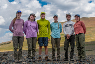 Group of researchers, including Brooke Wallasch (fourth from left), a Cal Poly master’s student in biological sciences, and Professor Dena Grossenbacher (far right) standing outdoors in a rocky alpine landscape with mountains visible in the background.