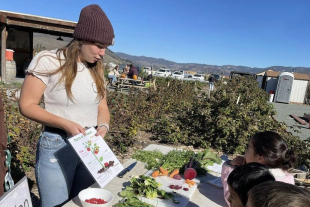 Cal Poly nutrition major Rairaja Cohen teaches young students about parts of a plant during an outdoor garden activity.