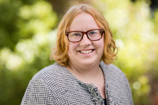 Chemistry Professor Ashley McDonald smiles in an outdoor portrait with green foliage in the background.