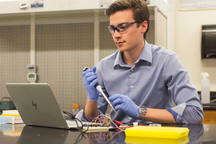 Brandon Strong analyzes experimental results in the lab holding pipette and looking at computer.