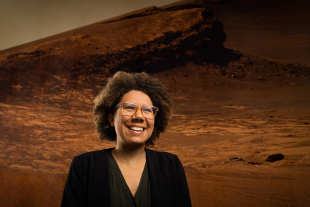 Astronomy professor Louise Edwards stands in front of a large wall mural showing the surface of Mars inside the Baker Center for Science and Mathematics.
