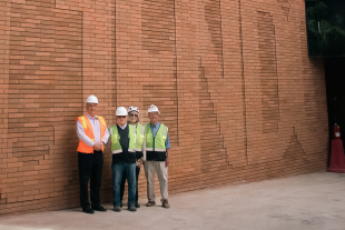 Cal Poly President Jeffrey D. Armstrong, Bill and Linda Frost, and Phil Bailey stand outside the Frost Center beside a tall brick wall spelling “Discere Faciendo.”