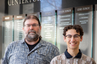 Mathematics Professor Charles David Camp and student Rapha Coutin standing in front of donor wall Cal Poly’s Center for Science and Mathematics.